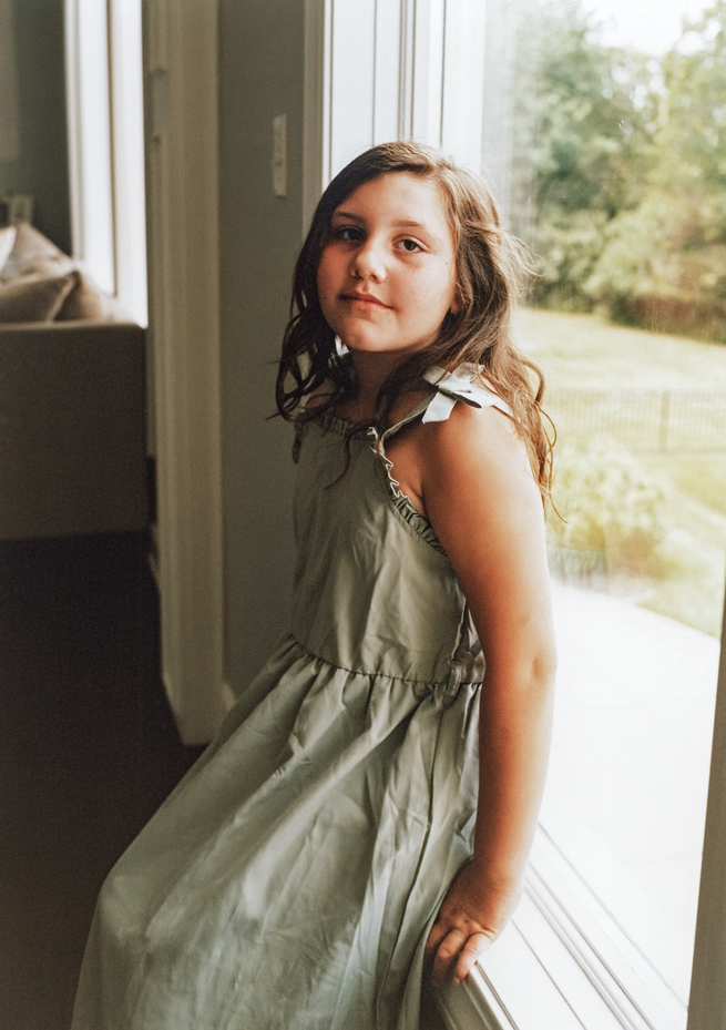 photo of girl with long hair in sundress sitting by window