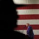 Trump speaking in front of a shadow over the American flag