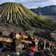 People climb a steep staircase up the side of a mountain, with a volcano in the background.