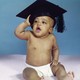 A baby clad in only a diaper holds a graduation cap on his head with an open-mouthed expression