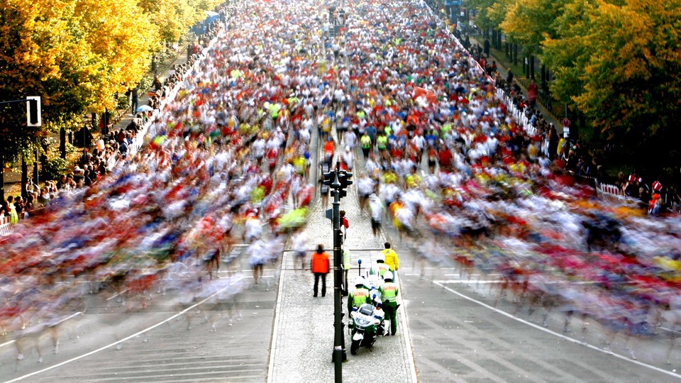 A wide street full of runners, splitting around a fork in the road. The runners in front are moving so quickly that many of them are blurs.