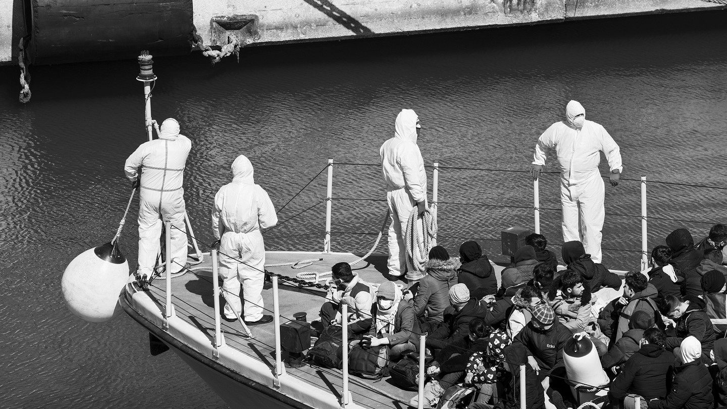 Italian law enforcement and a group of migrants gathered on the prow of a ship