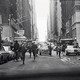 black-and-white photo of NYC street with people running alongside cars