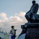 A girl reading a book walks by a statue of Dostoyevsky.