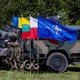 Soldiers stand next to tanks and the NATO flag