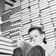 A sitting child reads a book, surrounded by tall stacks of other books