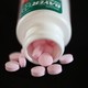 A bottle of Bayer aspirin spills pink pills labeled "Bayer"