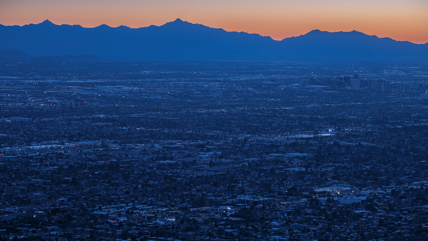 photo of blue-lit urban area at dawn or dusk with blue mountain ridge in background and orange sky