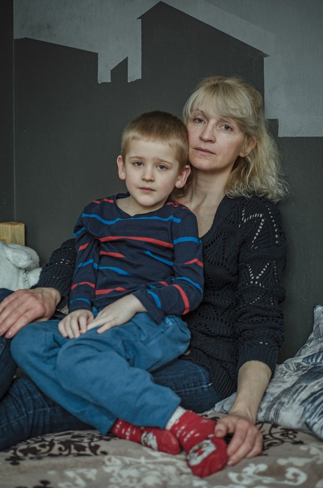 A small blond boy in striped shirt sits on a blonde woman's lap