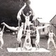 A black-and-white photo shows a team of 11 gymnasts posing in variously difficult stances, forming a symmetric scene.