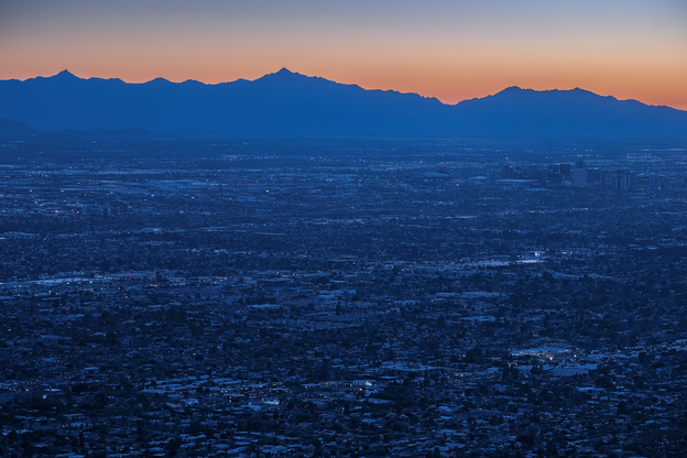photo of blue-lit urban area at dawn or dusk with blue mountain ridge in background and orange sky