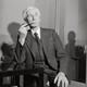 A black-and-white portrait of Bertrand Russell in a three-piece striped suit, smoking a pipe