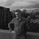 BW image of a man on a rooftop looking at the camera with his hand on his hip