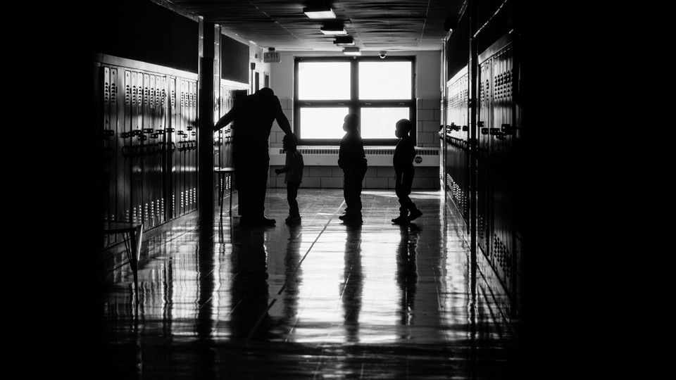 A black-and-white photograph of schoolchildren waiting in a hallway line to enter a classroom