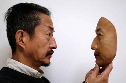 A man holds a realistic replica of a face.