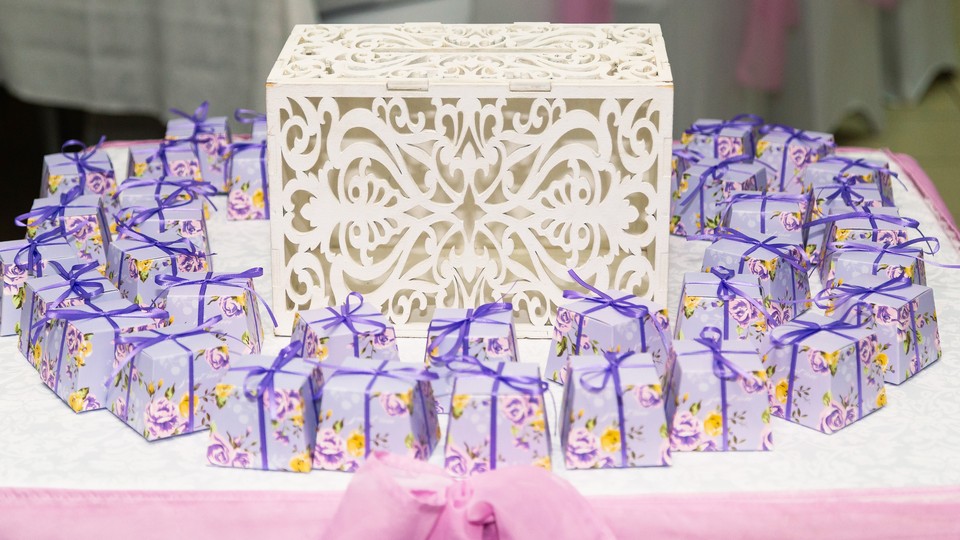 An ornate box sits on a table surrounded by small packages wrapped in floral paper and ribbon tied in a bow.