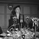 Eleanor Roosevelt stands behind a decorated table, behind several microphones.