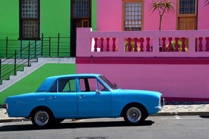 A bright blue car parked in front of pastel pink and green buildings