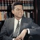 A photograph of John F. Kennedy sitting against a bookshelf