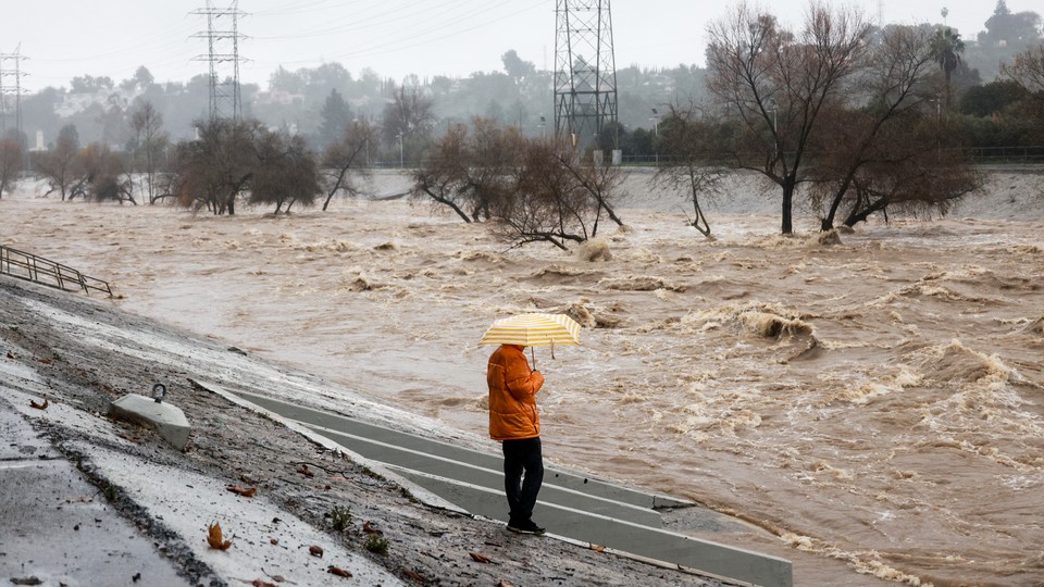 Photo of a person holding an umbrella beside the Los Angeles River during heavy rains