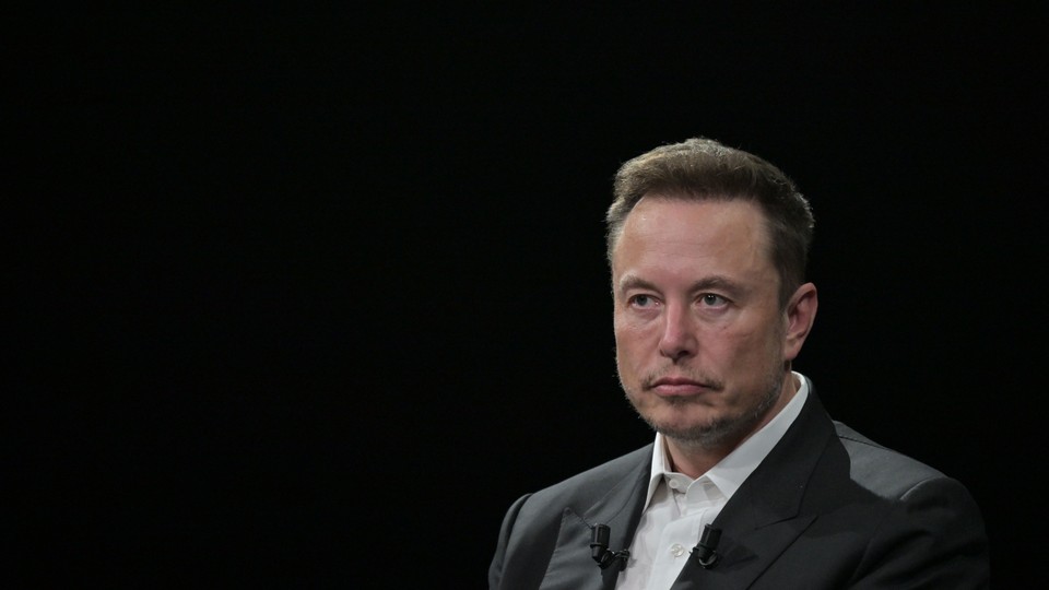 Elon Musk sits in front of a black background