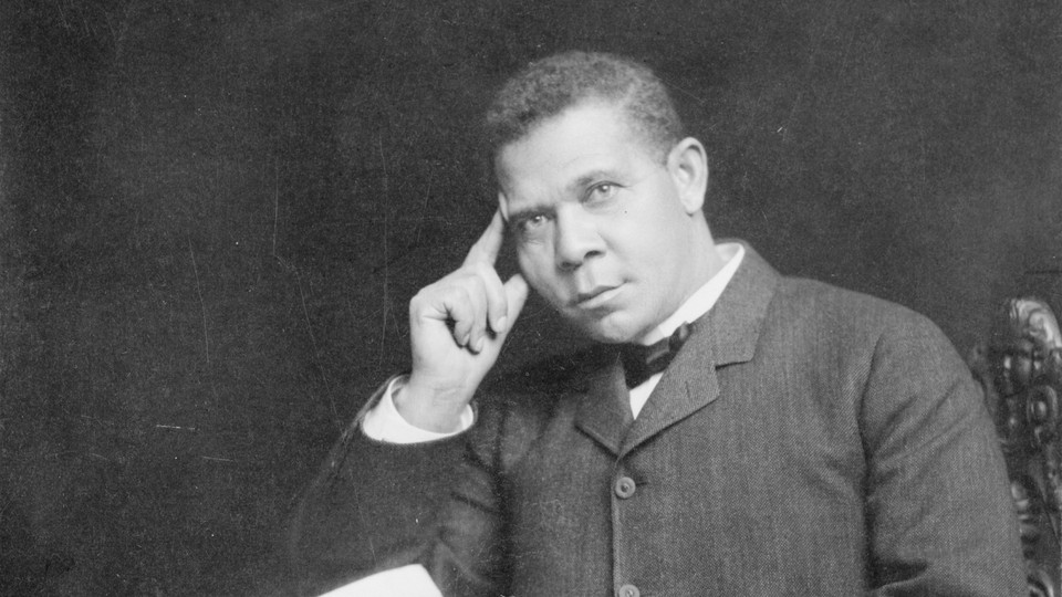 Black-and-white photograph of Booker T. Washington sitting at a desk, holding a paper