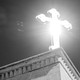 A cross on a rooftop, the sun illuminating it from behind