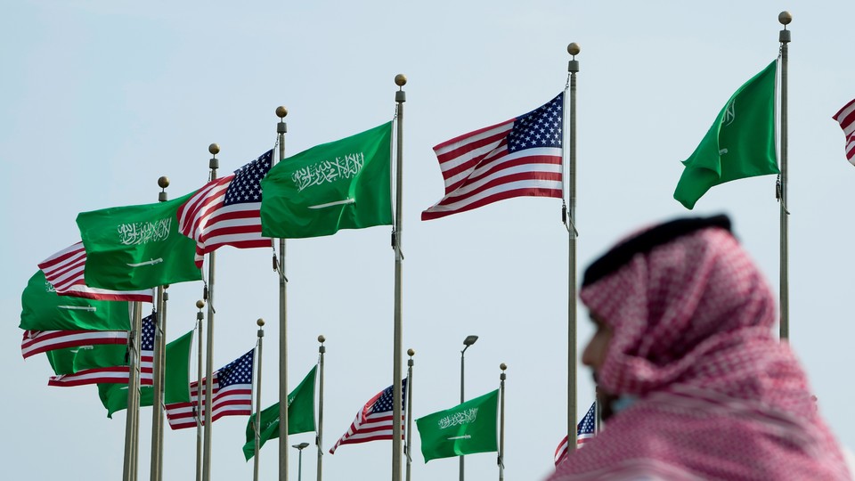 A man stands under American and Saudi flags