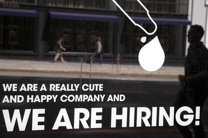 A man walks by a window with a hiring ad printed on it.