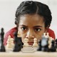 A young girl studies a chess board intently.