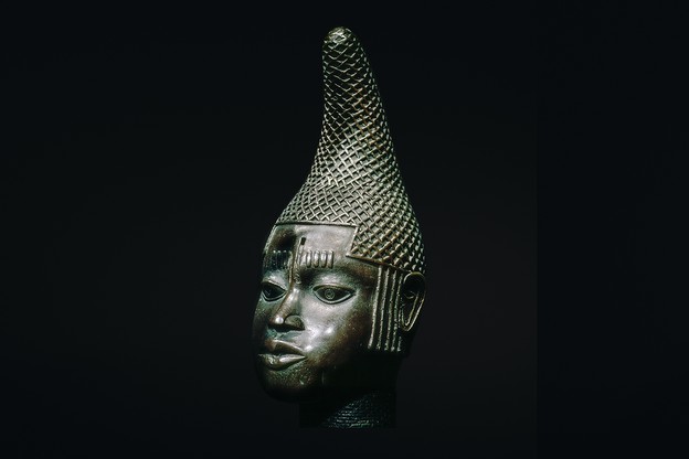 photo of a sculpture of a head with detailed conical headdress on black background