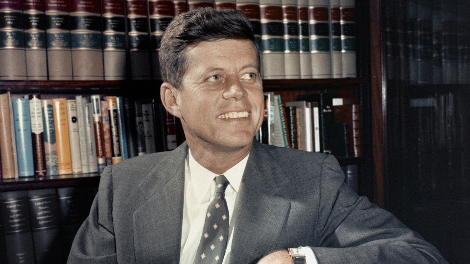 A photograph of John F. Kennedy sitting against a bookshelf