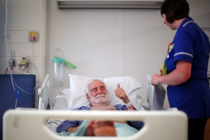 A man giving the "thumbs-up" sign in a British hospital bed