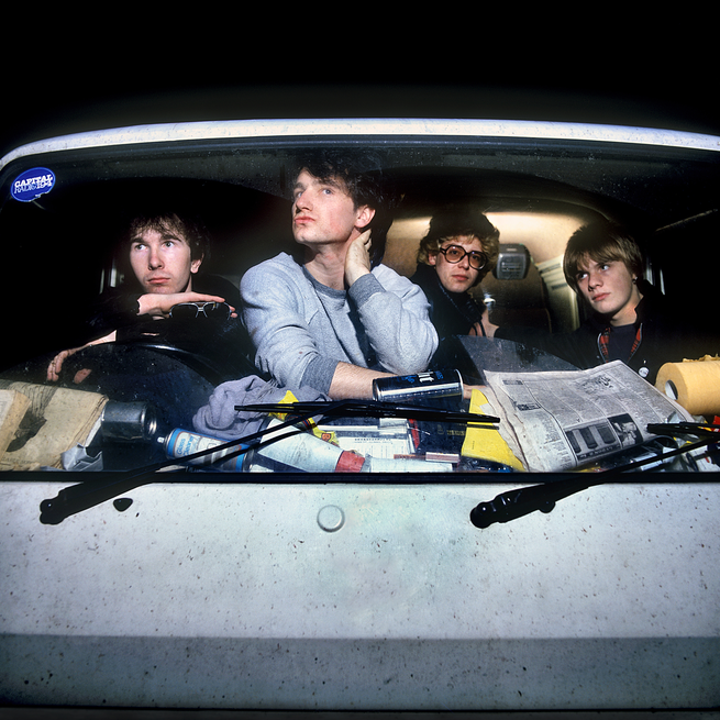 color photo of band members inside front windshield of van with cluttered dashboard