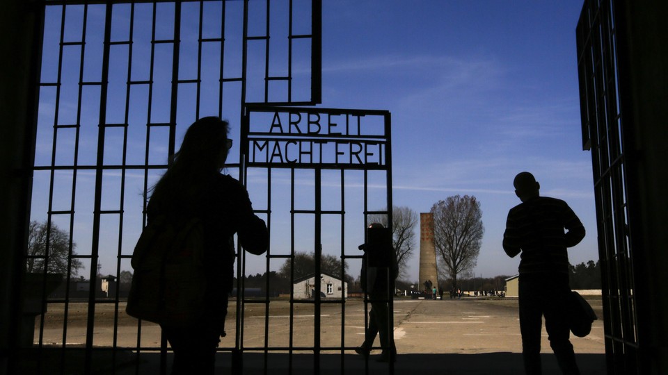Visitors enter Sachsenhausen through a gate with the words "Arbeit macht frei" (works sets you free).