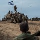 In the desert near the Israel-Gaza border, a tank with soldiers atop and alongside flies the Israeli flag.