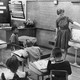 A black and white photograph of a teacher at the front of a classroom pointing to a dial on an antennae television