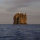 A small isolated island with tall sheer cliffs, topped by a lighthouse