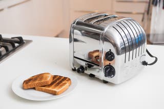 The shiny chrome Dualit NewGen toaster, a model we tested to find the best toaster, next to a plate of toast showing burnt and raw stripes.