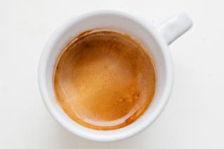 Top view of a small white espresso cup with rich golden espresso in it.