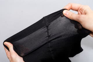 Two hands stretching the waistband on a pair of black Wolford Merino Tights.