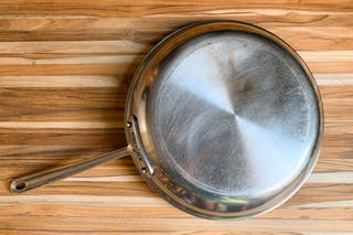 The bottom of a used All-Clad skillet, viewed from above, showing some scratches.