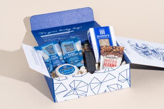 The contents of Jasper Hill's The Vermonter box nestled among wood shavings inside a vibrant blue and white box.