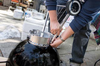 Someone attaching the legs to a Weber charcoal grill.