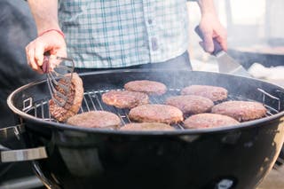 Someone flipping burger patties on a charcoal grill.