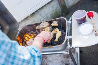 Someone grilling chicken on a charcoal grill.