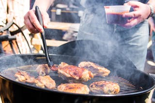 Someone brushing chicken with barbecue sauce on a charcoal grill.