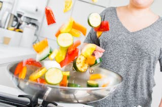 A person tossing sliced vegetables in the All-Clad skillet.