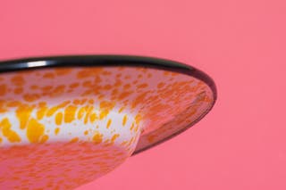 A closeup of the underside of the rim of a white and yellow speckled Red Co. Enamelware Dinner Plate.