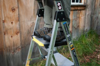 A person's feet on the top step of the Gorilla GLX-5B stepladder.